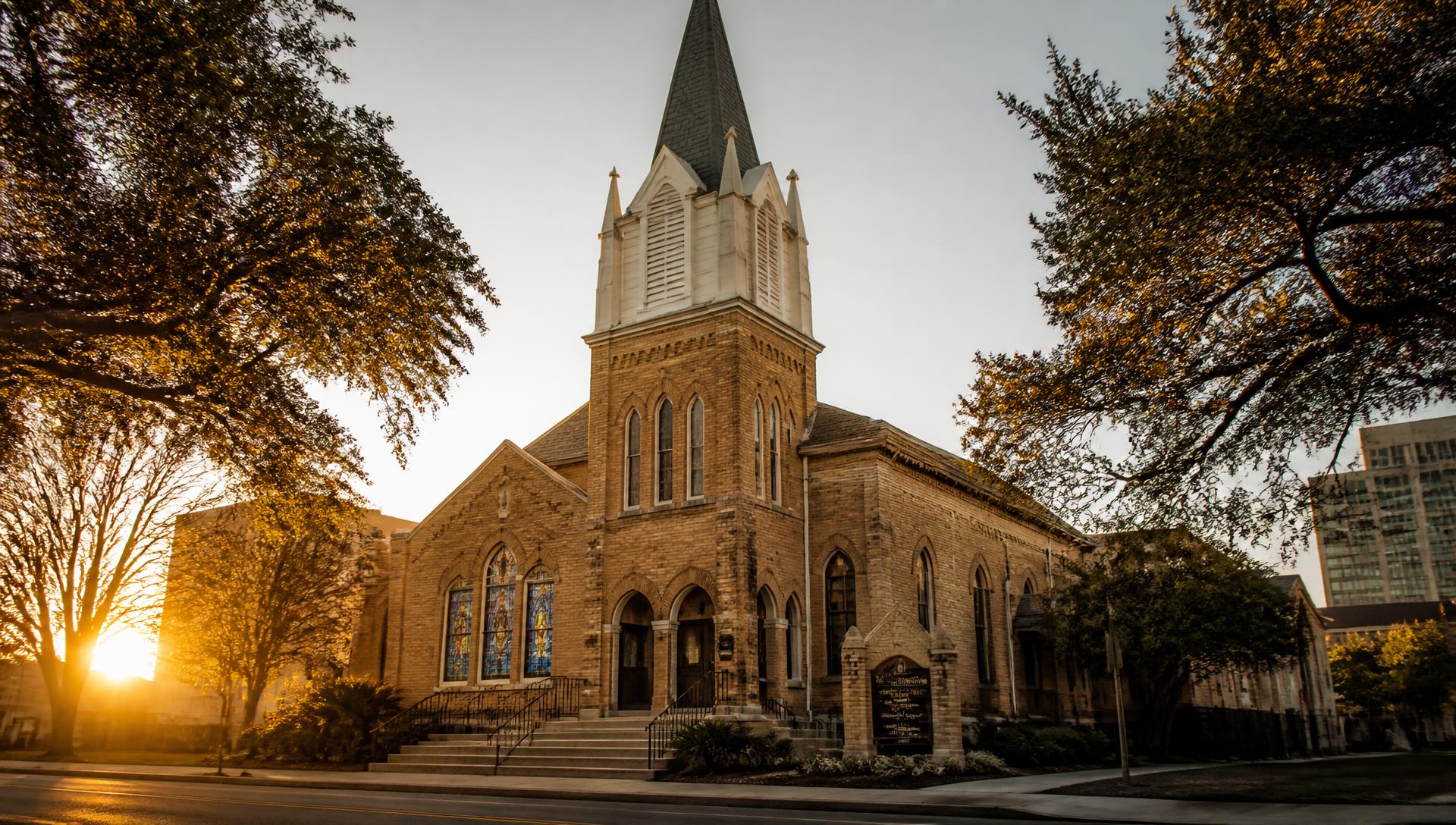 Historic brick church with a white steeple in San Antonio at golden hour